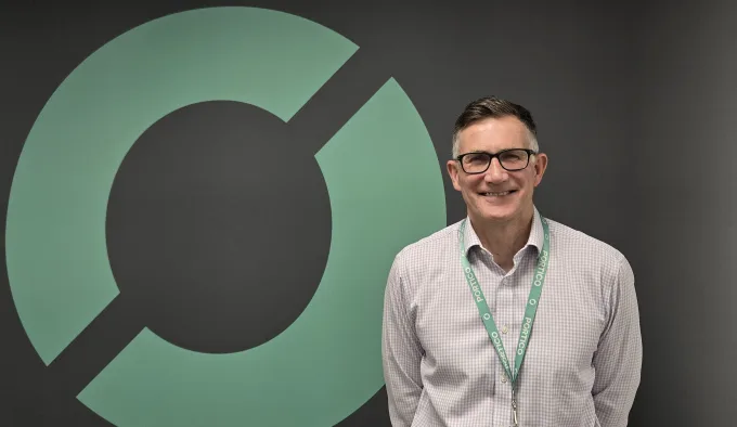A picture of Simon Clarke, standing in front of a wall bearing the Portico shipping logo